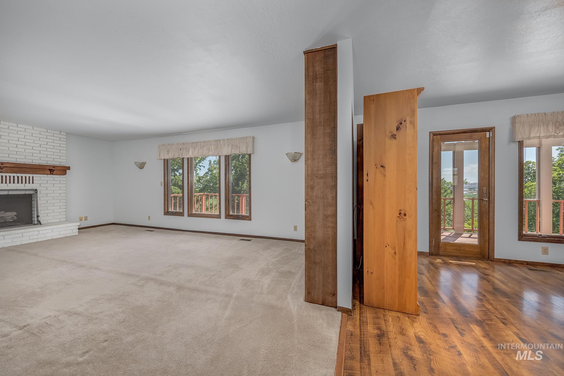 1493 Cove Road Weiser, ID 83672 - Photo 13 of 50 Spacious interior featuring a white brick fireplace with wood mantel, multiple windows, a glass-paned door, wood-finish flooring, and a carpeted area