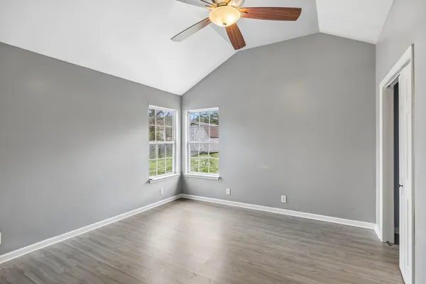 an empty room with wooden floor chandelier fan and windows