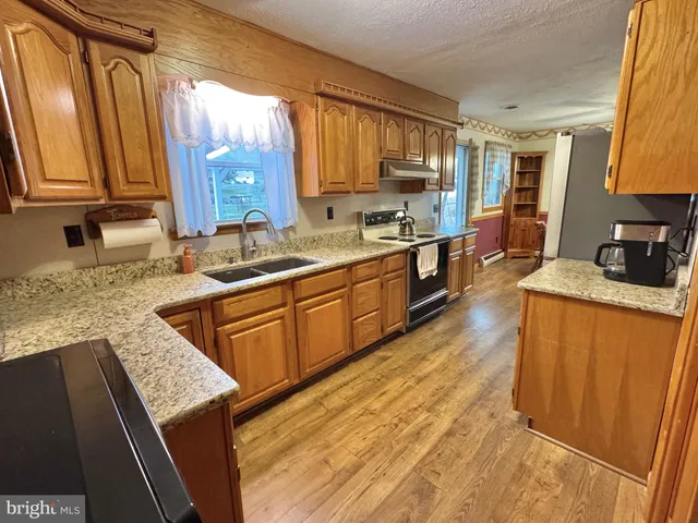 a kitchen with stainless steel appliances granite countertop wooden cabinets a sink dishwasher a stove and a refrigerator with wooden floor