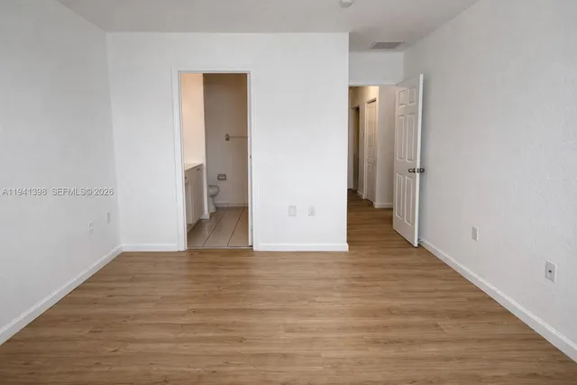 a view of an empty room with wooden floor and a bathroom