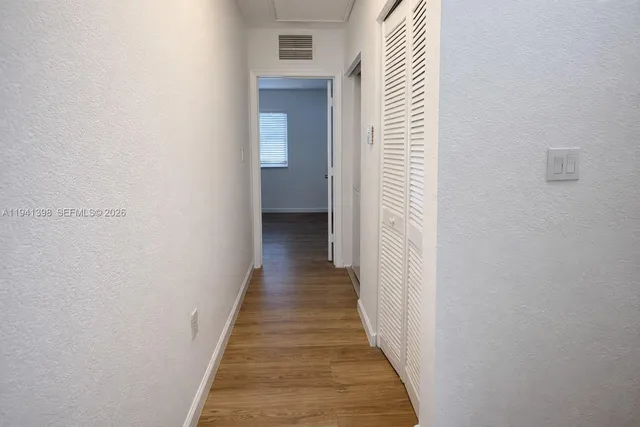 a view of a hallway with wooden floor and a bathroom