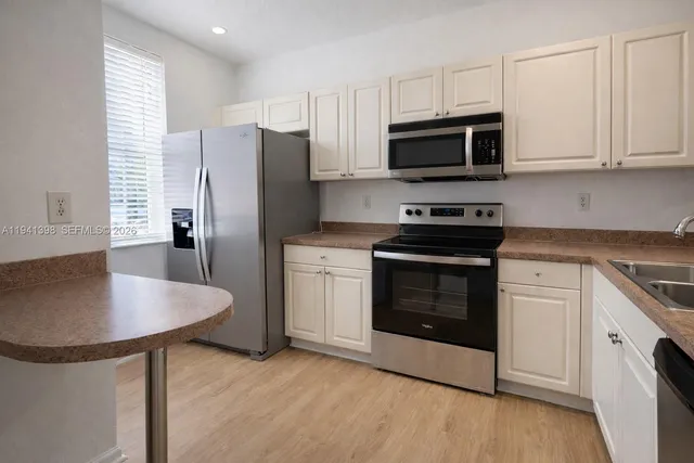 a kitchen with stainless steel appliances a stove a microwave a refrigerator a sink and white cabinets