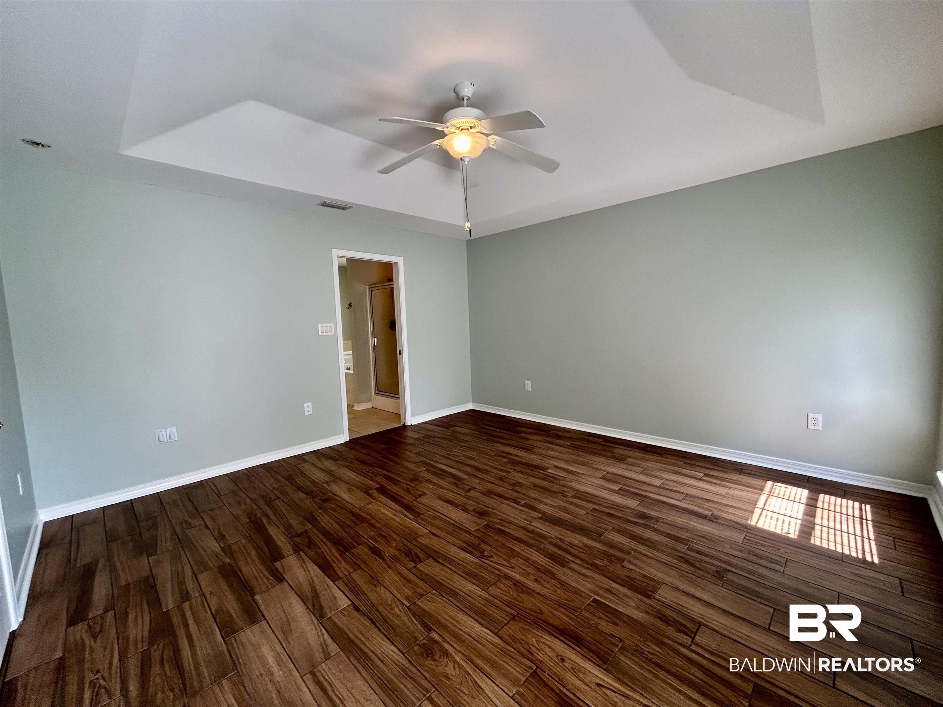 7198 Raintree Lane Gulf Shores, AL 36542 - Photo 12 of 33 Spacious room featuring wood-finish flooring, a tray ceiling, and a ceiling fan with integrated lighting