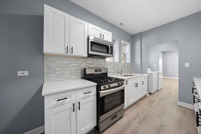 a kitchen with stainless steel appliances granite countertop white cabinets a sink a stove and a microwave