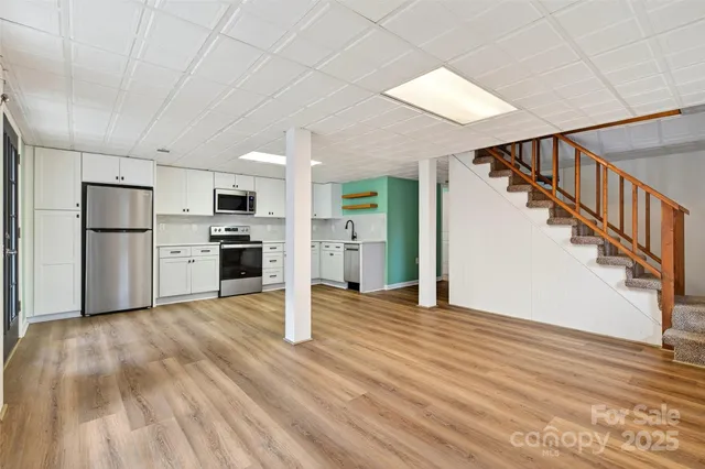 a view of a kitchen with wooden floor electronic appliances and stairs