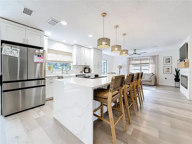 a kitchen with stainless steel appliances kitchen island granite countertop a refrigerator a stove a dining table and chairs with wooden floor