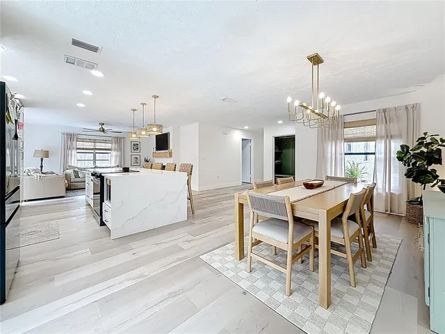 a living room with a dining table wooden floor and a kitchen view