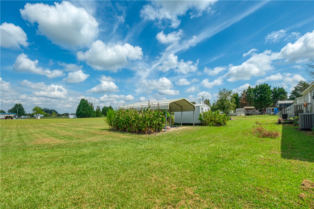 1905 Bethany Church Road Belton, SC 29627 - Photo 18 of 20 An open grassy lawn surrounds a metal carport structure and storage shed under blue skies.
