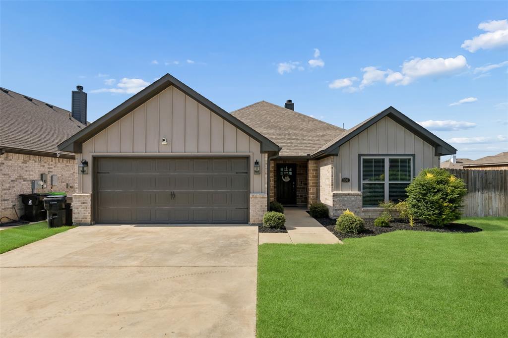 108 Maverick Lane Pilot Point, TX 76258 - Photo 1 of 27 Contemporary single-story residence with a tan brick and stone facade, vertical board-and-batten siding, and a gabled roofline