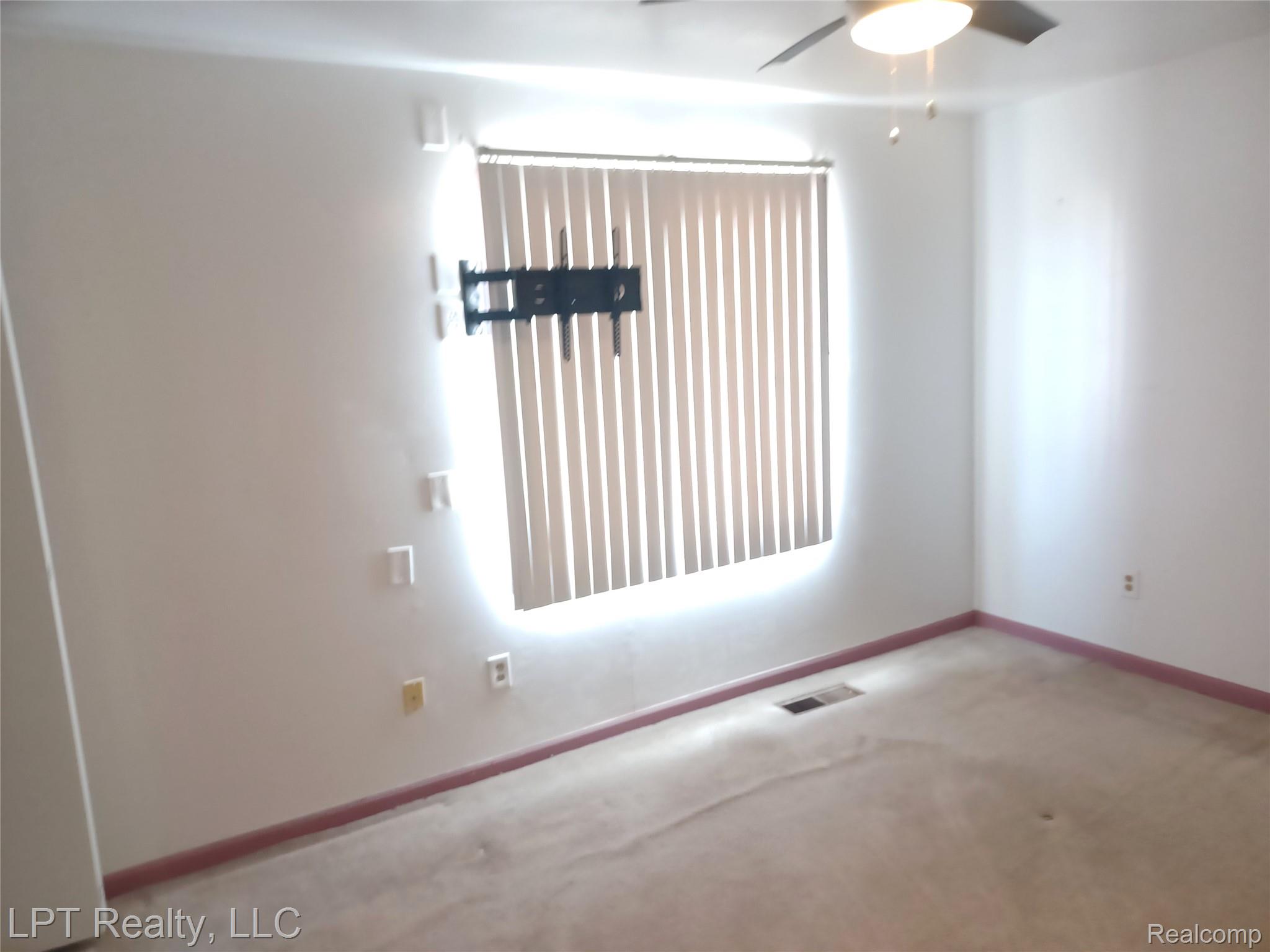 3304 Spinnaker Lane, Unit 47 Detroit, MI 48207 - Photo 11 of 21 Window with vertical blinds, wall-mounted television bracket, ceiling fan with integrated lighting, and neutral carpeted flooring