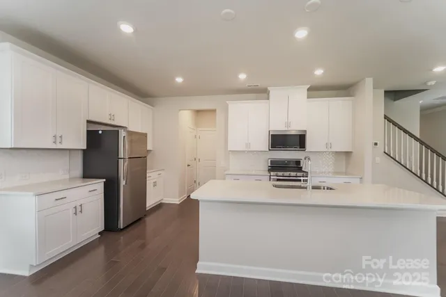 a kitchen with stainless steel appliances kitchen island granite countertop a refrigerator a sink dishwasher a stove with white cabinets and wooden floor