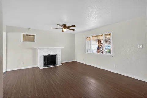 a view of an empty room with wooden floor fireplace and a window