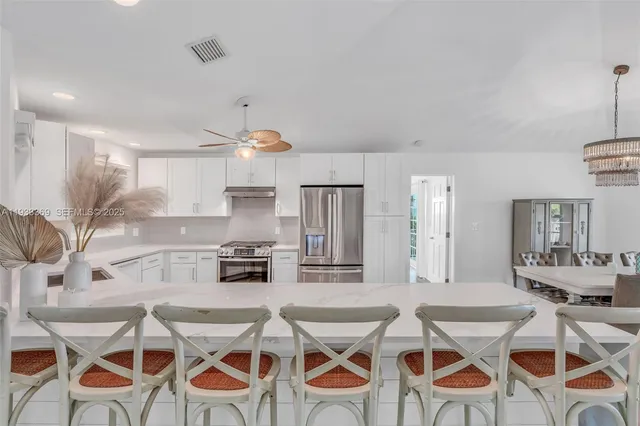 a kitchen with stainless steel appliances kitchen island granite countertop a dining table chairs and white cabinets