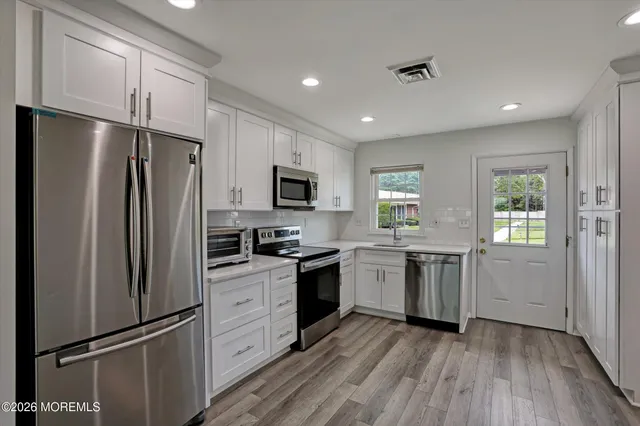 a kitchen with white cabinets stainless steel appliances a sink and a window