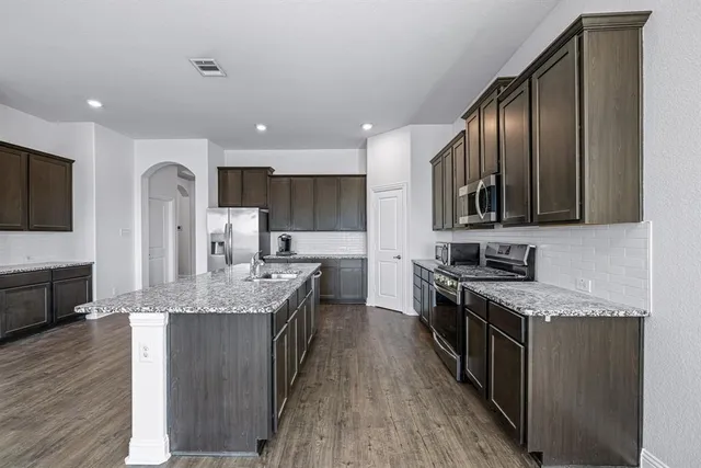 a large kitchen with a large counter top a sink stainless steel appliances and cabinets