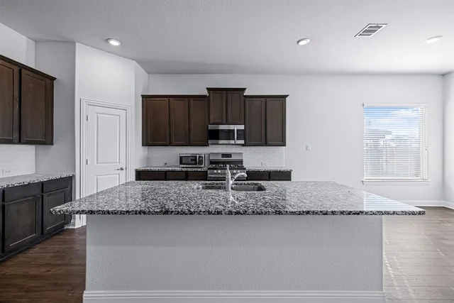 a large kitchen with stainless steel appliances granite countertop a stove a sink dishwasher a microwave oven and a refrigerator with wooden floor