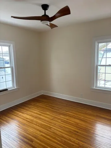 an empty room with wooden floor fan and windows