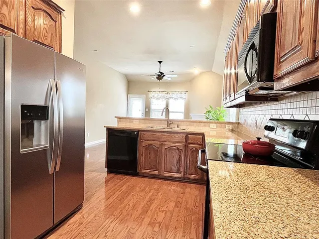 a kitchen with stainless steel appliances granite countertop a refrigerator a stove and a sink with wooden floors