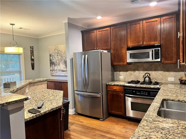 a kitchen with stainless steel appliances granite countertop a refrigerator a sink dishwasher a stove and a dining table with wooden floor