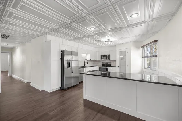 a kitchen with stainless steel appliances granite countertop a refrigerator a sink dishwasher a stove and white countertops with wooden floor