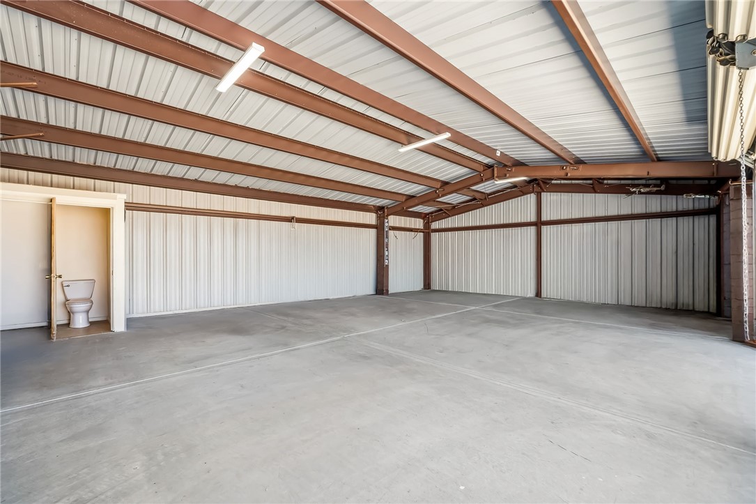 10809 North Jemez Road Kingman, AZ 86401 - Photo 15 of 51 Spacious metal structure featuring a high corrugated ceiling with exposed brown steel beams, concrete flooring, and fluorescent lighting