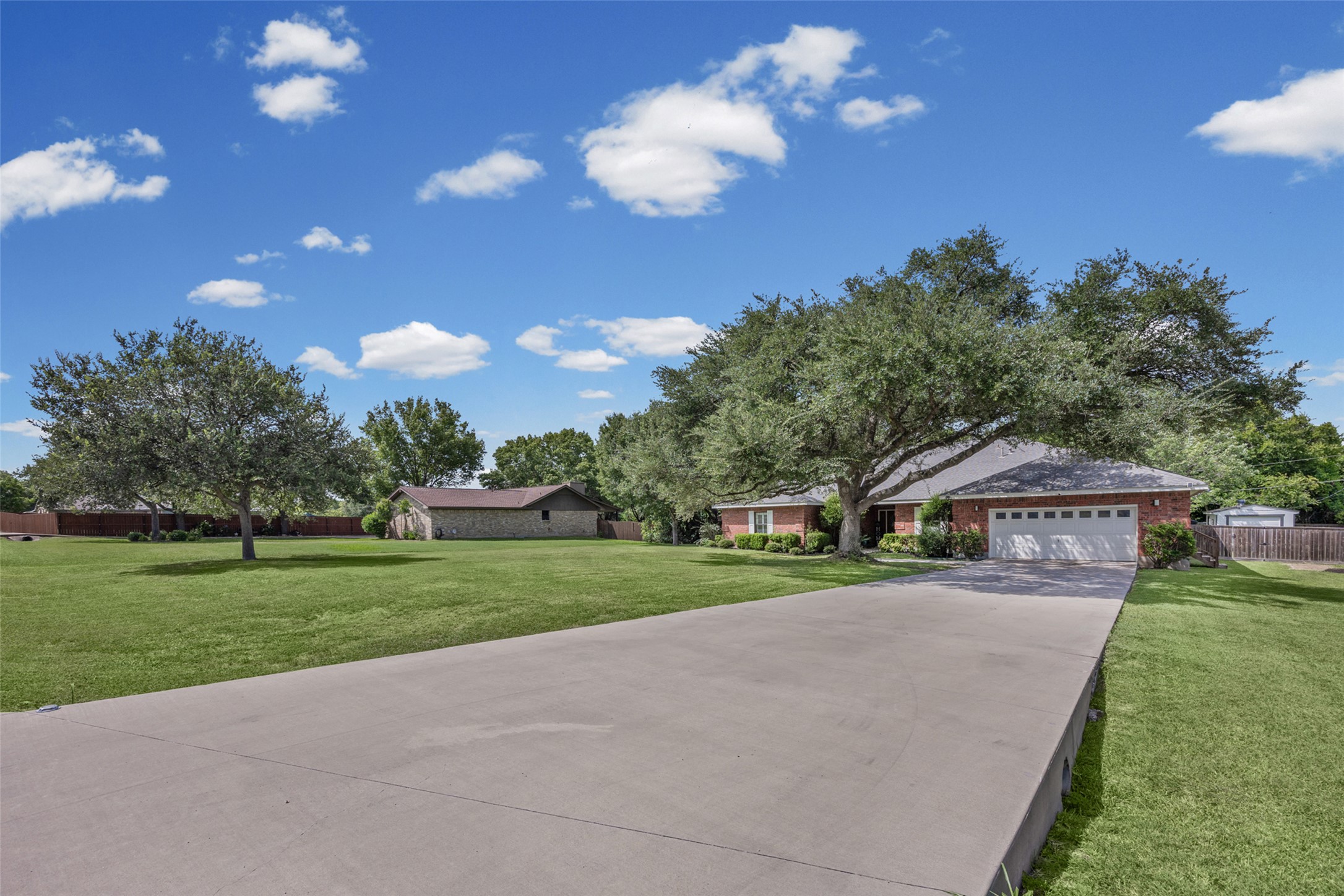 2000 Spinel Road Pflugerville, TX 78660 - Photo 2 of 31 A long concrete driveway leads to a brick residence with an attached garage, surrounded by mature trees.
