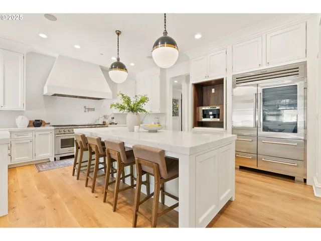 a kitchen with stainless steel appliances kitchen island granite countertop a stove a refrigerator a sink a dining table and chairs with wooden floor