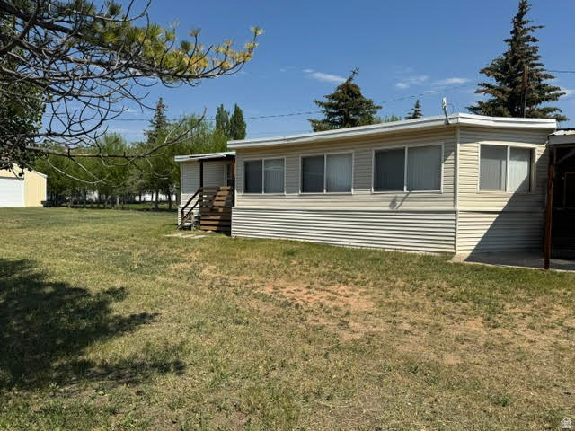 123 North 3rd Manila, UT 84046 - Photo 3 of 15 Spacious property featuring a light-colored mobile home with horizontal siding, multiple windows, and a raised wooden entry deck with stairs