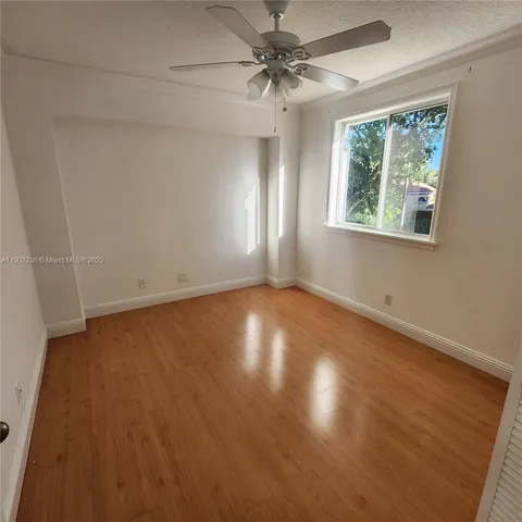 an empty room with wooden floor chandelier fan and windows