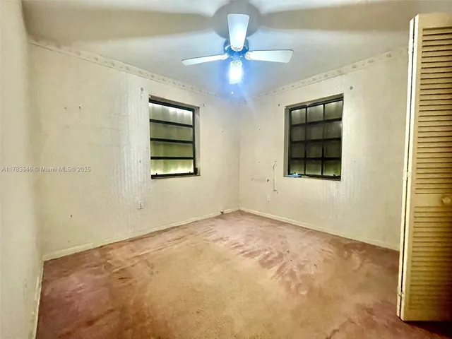 an empty room with chandelier fan and windows