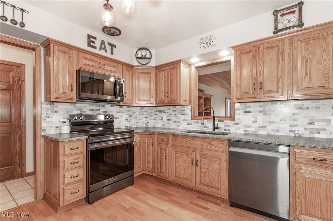 2866 South County Line Road Madison, OH 44057 - Photo 24 of 48 Kitchen with stainless steel appliances, decorative backsplash, dark stone counters, a sink, and light wood-style flooring