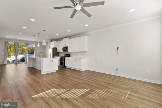 a view of an empty room and kitchen view with wooden floor