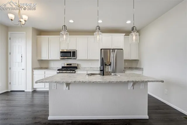 a kitchen with stainless steel appliances granite countertop a refrigerator a sink dishwasher a stove and white cabinets with wooden floor