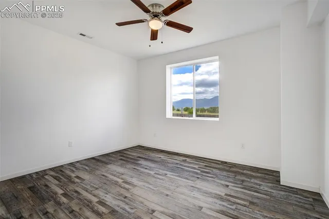 an empty room with wooden floor ceiling fan and windows