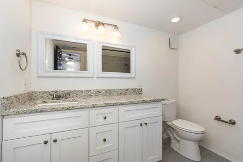 a bathroom with a granite countertop toilet sink and mirror