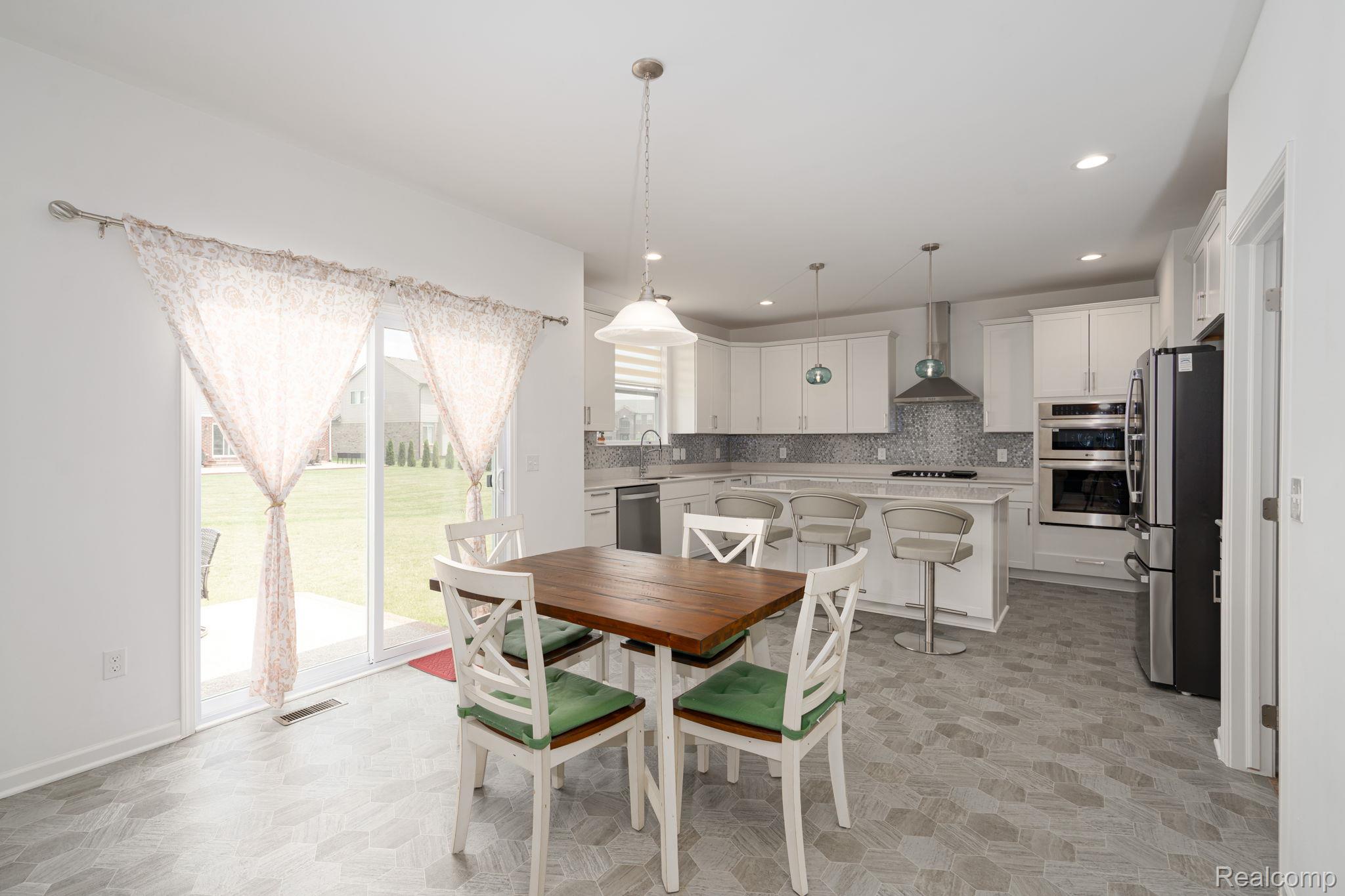 48904 Carnegie Way Macomb, MI 48042 - Photo 7 of 34 Modern kitchen featuring white cabinetry, stainless steel appliances, a tile backsplash, and an island with bar seating
