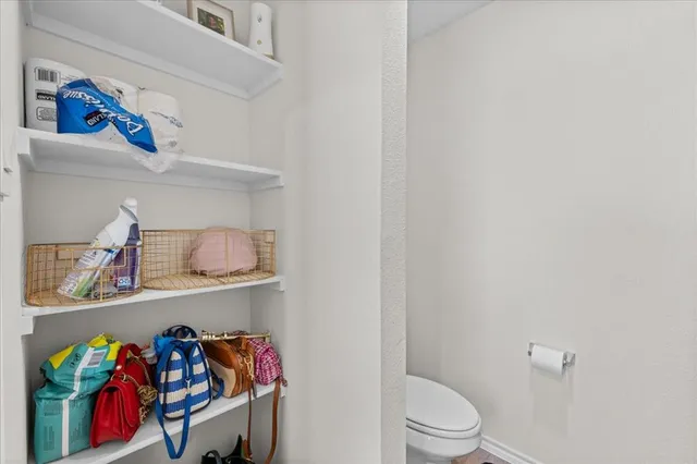 a white toilet sitting next to a shelf with clothes and shoes