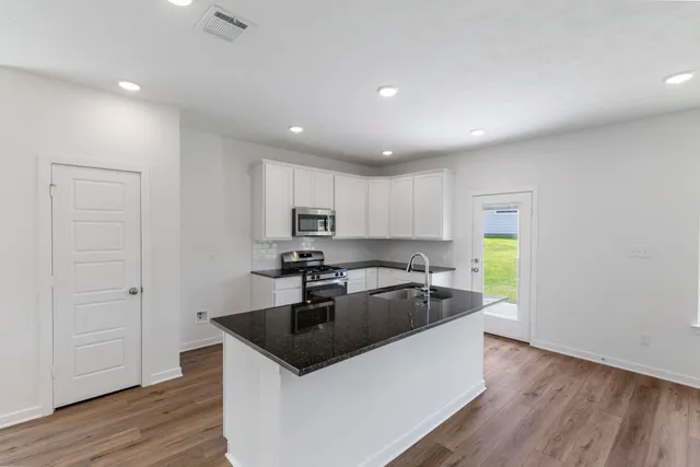 a kitchen with granite countertop stainless steel appliances a sink a stove a refrigerator cabinets and a window