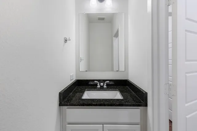 a bathroom with a granite countertop sink and white cabinets