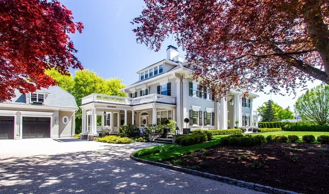 a view of a white house with a large tree and flower plants