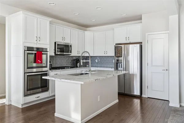 a kitchen with stainless steel appliances a microwave a stove a sink dishwasher a refrigerator and white cabinets with wooden floor