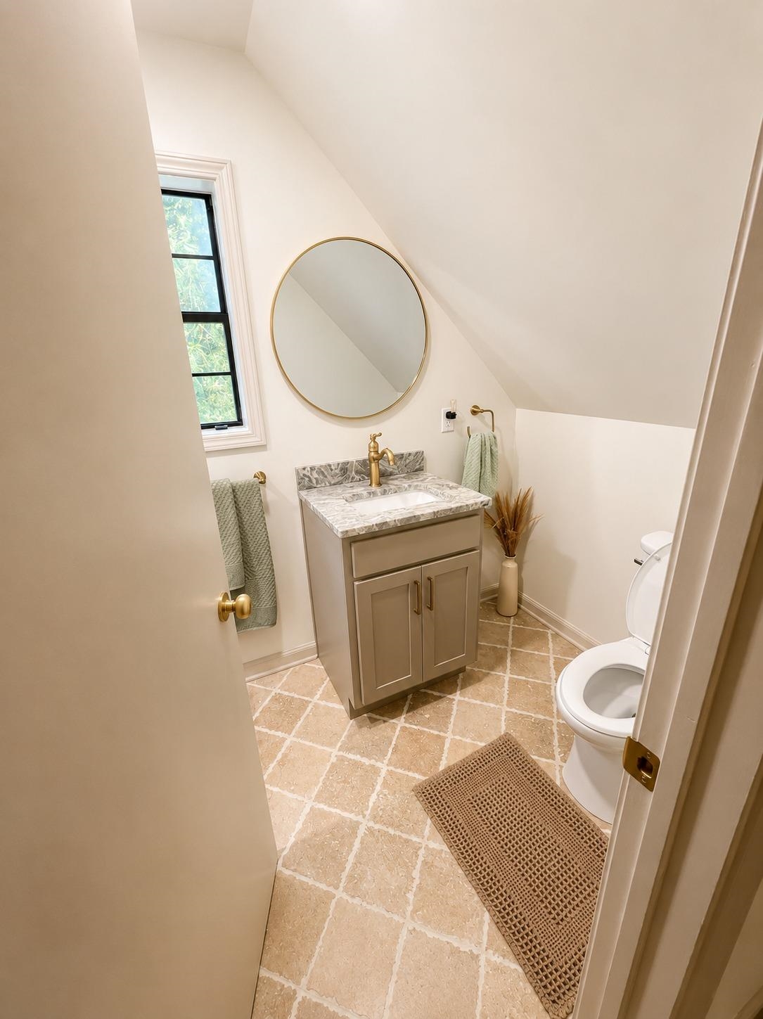 470 Rich Road Somerville, TN 38068 - Photo 38 of 40 Neutral-toned bathroom with an angled ceiling, featuring a vanity with a gray cabinet and a light-toned countertop, a round gold-framed mirror, and a window with dark trim
