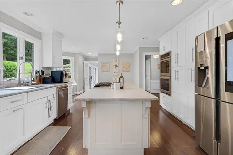 a kitchen with stainless steel appliances kitchen island granite countertop a refrigerator a sink dishwasher a oven and a dining table with wooden floor
