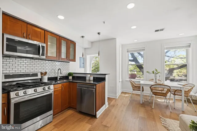 a kitchen with stainless steel appliances granite countertop a stove top oven a sink dishwasher and white cabinets with wooden floor