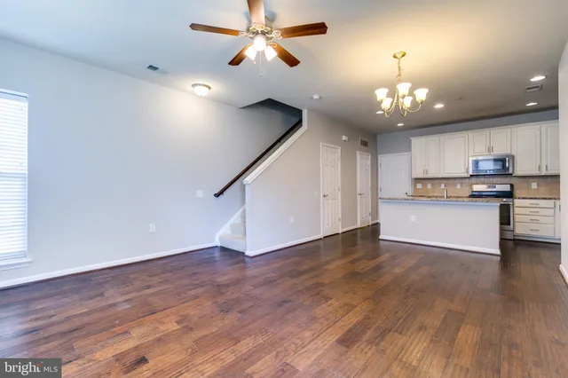 an empty room with wooden floor ceiling fan and kitchen view