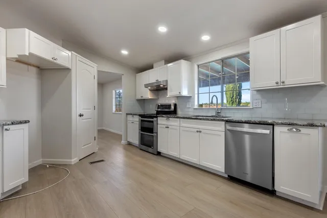 a kitchen with stainless steel appliances granite countertop a stove a sink and white cabinets