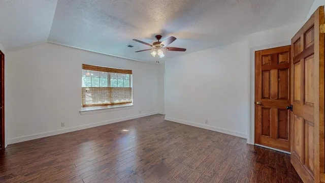 an empty room with wooden floor chandelier fan and windows