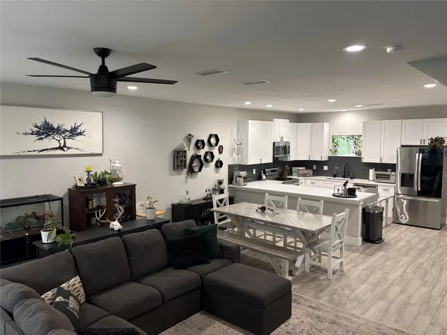 a view of living room kitchen with stainless steel appliances kitchen island granite countertop a couch a stove a sink a dining table and chairs with wooden floor