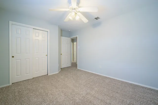 an empty room with a chandelier fan and closet area