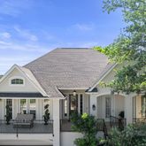 a view of a white house next to a yard with plants and trees